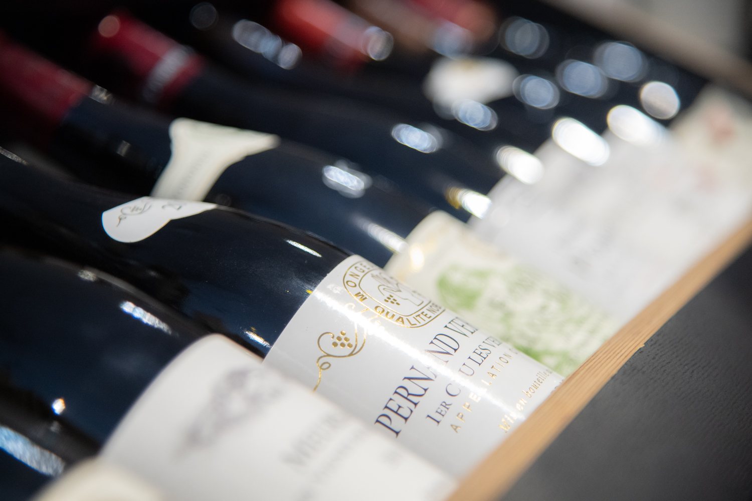 Gros plan sur des bouteilles de vin couchées sur une étagère en bois, avec une étiquette blanche de premier cru au premier plan et un arrière-plan flou.