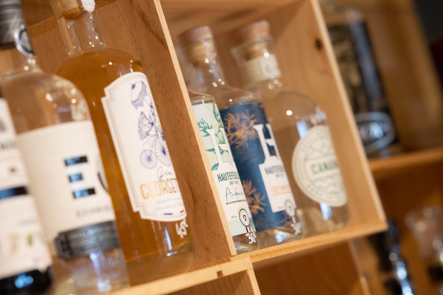 Plusieurs bouteilles de gin aux étiquettes colorées sont présentées dans des casiers en bois clair.