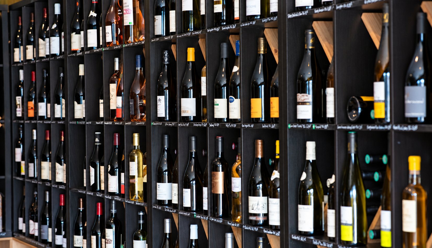 Un grand mur d'étagères noires à casiers présente de nombreuses bouteilles de vin rouge, blanc et rosé, étiquettes tournées vers l'avant.