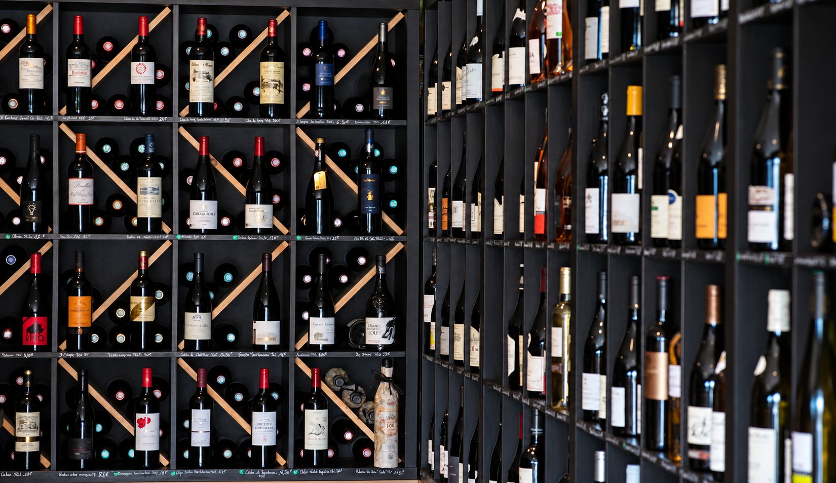 Des bouteilles de vin rouge, blanc et rosé sont rangées dans de grandes étagères noires à casiers, certaines posées en diagonale.