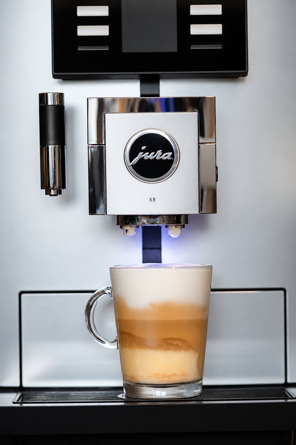 Une machine à café automatique Jura X8 en gros plan verse un latte macchiato en couches dans un verre transparent.