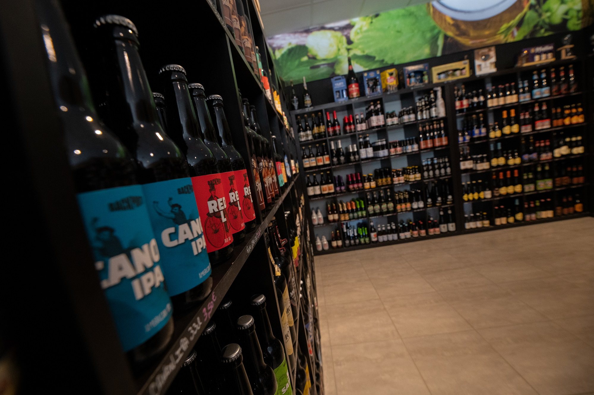 Dans un magasin spécialisé, des étagères sombres présentent de nombreuses bouteilles de bières artisanales, au premier plan des étiquettes bleues et rouges de type IPA.